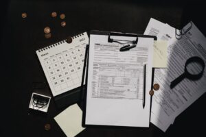 A person sitting at a kitchen table sorting through tax documents with a calculator and laptop.