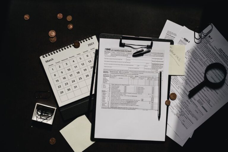 A person sitting at a kitchen table sorting through tax documents with a calculator and laptop.