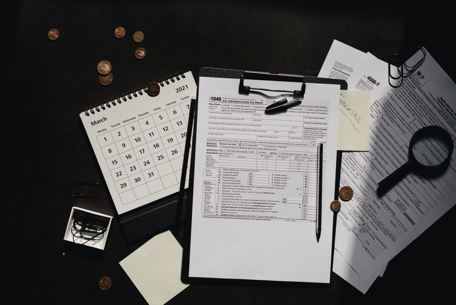 A person sitting at a kitchen table sorting through tax documents with a calculator and laptop.