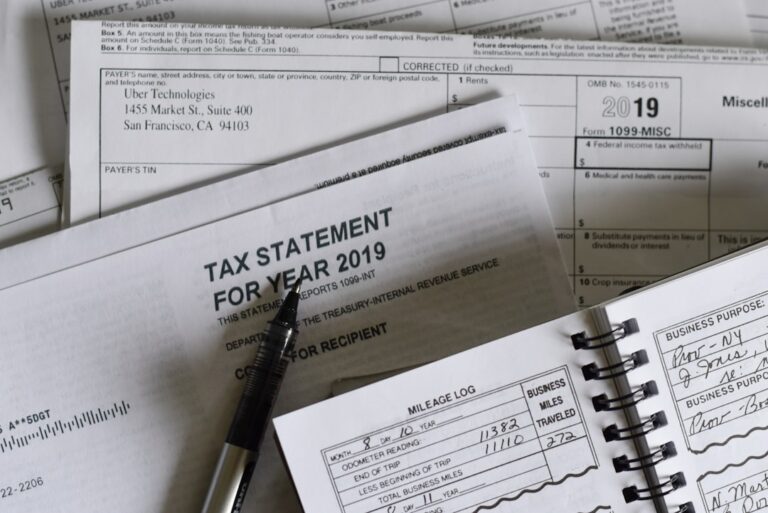 A person sitting at a kitchen table organizing tax forms with a laptop and calculator visible.